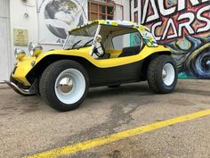 a yellow and black car parked in front of a building with graffiti on the wall