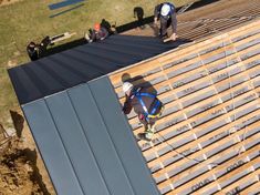 two men working on the roof of a building with metal shingles and wood slats