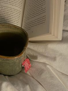 an open book on a bed next to a cup with a red tag in it