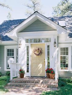 a white house with two potted plants on the front steps and a yellow door