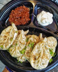 some dumplings are in a black bowl with sauce on the side and other food items