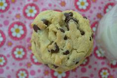 a cookie with chocolate chips is next to a jar of milk on a pink and white flowered tablecloth