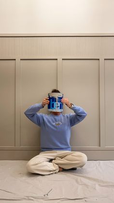 a person sitting on the ground holding up a box over their head with both hands