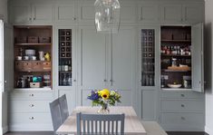 a dining room table and chairs in front of gray cabinets with glass vases on them