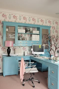 a home office with blue cabinets and floral wallpaper on the walls, along with a computer desk