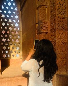 a woman taking a photo with her cell phone in front of an intricately carved wall