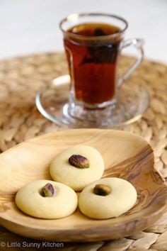 three cookies on a wooden plate next to a cup of tea