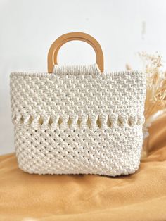 a white crocheted bag with wooden handle sitting on top of a bed next to dried grass