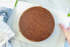 a cake sitting on top of a white plate next to a person's hand