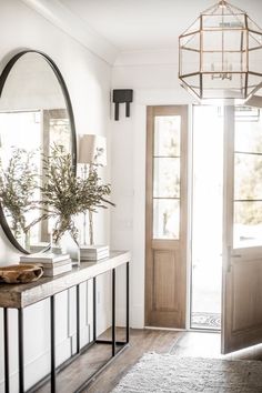 an entryway with a mirror, vases and plants on the consoleor table