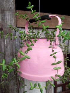 a pink watering can with green plants growing out of it's side hanging from a wooden fence