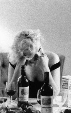 a woman sitting at a table with two bottles of wine in front of her face