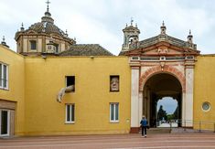 a person walking in front of a yellow building with an arch and clock on it