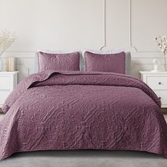 a bed with a purple comforter and two pillows on top of it in a white room