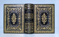 an open book with black and gold designs on the front, sitting on a white surface