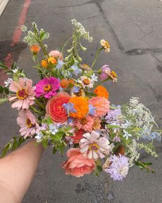 a person holding a bouquet of flowers in their hand on the side of the road