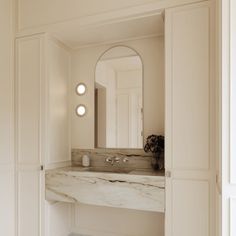 a white bathroom with marble counter top and vanity mirror above it, along with two lights on either side of the sink