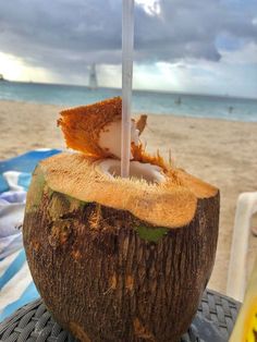 a coconut drink sitting on top of a wooden table next to the ocean with a straw sticking out of it