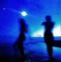 two people standing in front of a blue light with their hands on their hipss