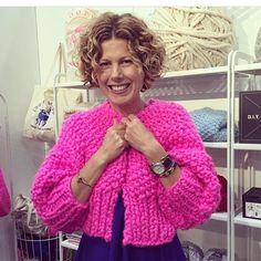 a woman standing in front of a display of knitted sweaters and scarves