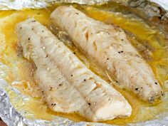 two fish fillets sitting on top of tin foil in a pan with oil and seasoning