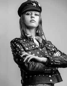 a woman in a leather jacket and hat with her arms crossed, looking at the camera