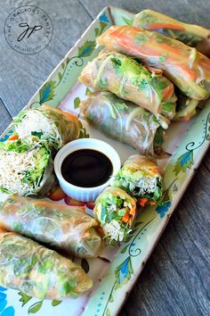 an assortment of vegetable spring rolls on a plate with dipping sauce and garnishes