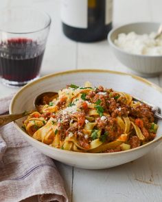 a white bowl filled with pasta and meat next to a glass of wine on a table