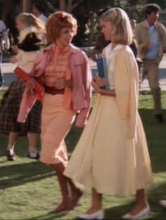 an old photo of two women talking to each other on the grass with people in the background