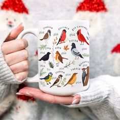 a person holding a coffee mug with birds on it in front of red and white christmas decorations