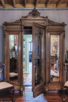 an ornate wooden armoire with mirrored doors in a living room next to a chair