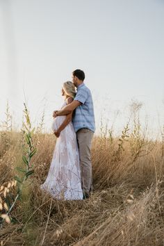 a man and woman standing in the middle of a field with tall grass on each side