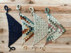 three pieces of crocheted cloth hanging from hooks on a wooden surface with scissors