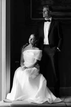 a man and woman in formal wear standing next to each other by a doorway, black and white photograph