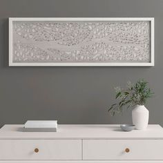 a white vase sitting on top of a dresser next to a wall mounted art piece