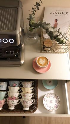 a coffee maker sitting on top of a white counter next to cups and saucers