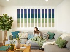 a woman sitting on top of a couch in a living room next to a potted plant