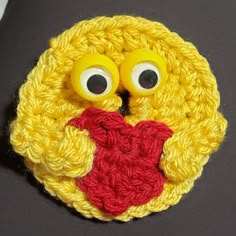 a crocheted brooch with googly eyes and a red heart on it