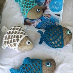 four fish made out of knitted material sitting on top of a white blanket next to a magazine