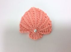 a crocheted pink flower with a pearl in the center on a white background