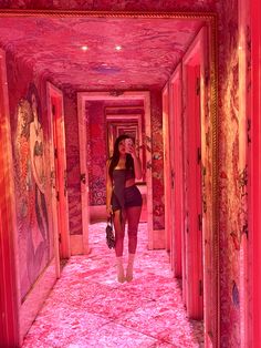 a woman walking down a long hallway covered in pink carpeted walls and flooring