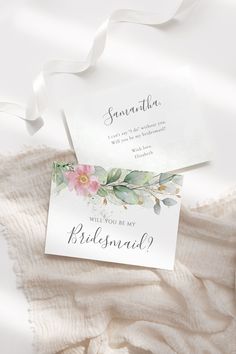 the wedding stationery is laid out on top of a white blanket with flowers and greenery