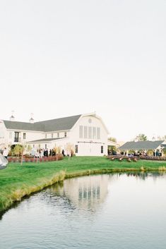 a large white house sitting on top of a lush green field next to a lake