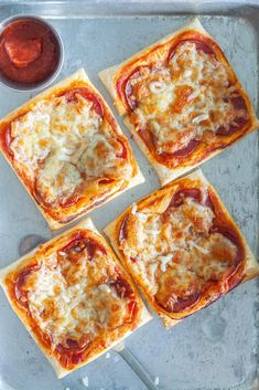 four square pizzas with cheese and sauce on a baking sheet, ready to go into the oven