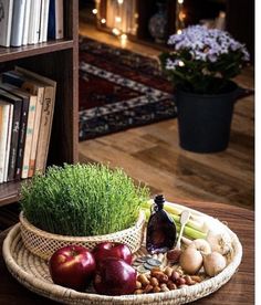 an assortment of fruits and vegetables sitting on a table in front of a bookshelf