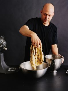 a man in black shirt preparing food on top of a metal pot and pans