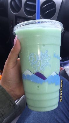 a person holding up a green drink in their hand while sitting in the backseat of a car