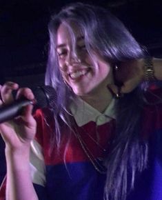 a woman with long hair holding a microphone in her hand and smiling at the camera