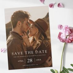 a wedding photo save the date card with pink flowers and greenery next to it