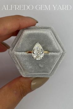 a hand holding an engagement ring in a velvet box with the words, alfredo gems yard